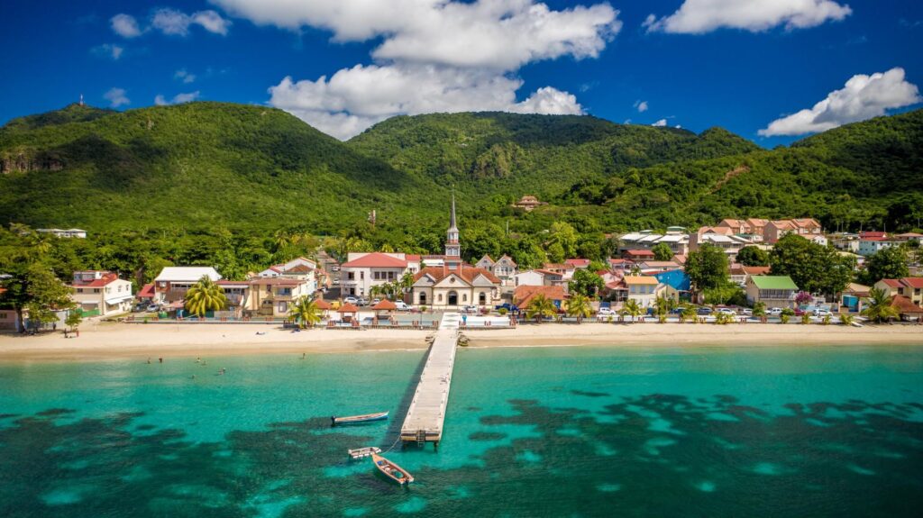 Paysage de Martinique avec mer turquoise, village côtier et montagnes tropicales.
