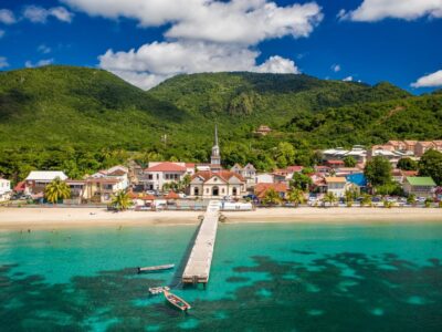 Paysage de Martinique avec mer turquoise, village côtier et montagnes tropicales.